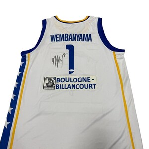 May include: White basketball jersey with blue and yellow trim. The jersey features the name "WEMBANYAMA" above the number "1" and a signature. The team name "BOULOGNE-BILLANCOURT" is also visible.