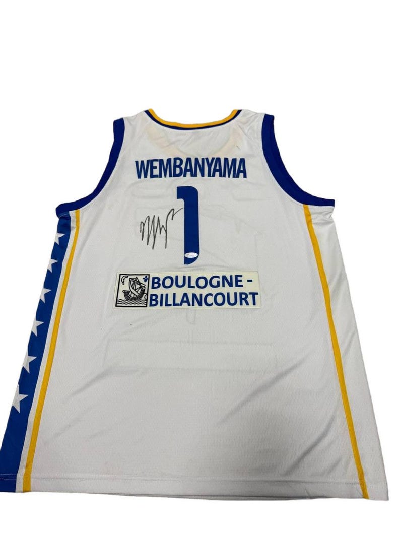 May include: White basketball jersey with blue and yellow trim. The jersey features the name "WEMBANYAMA" above the number "1" and a signature. The team name "BOULOGNE-BILLANCOURT" is also visible.