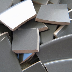 May include: A pile of broken gray ceramic tiles with white edges.