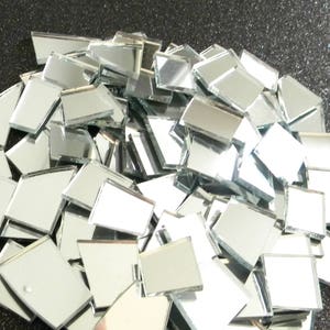 May include: A pile of small, square, silver mirror tiles. The tiles are arranged in a random pattern and are all the same size.