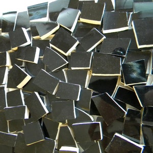 May include: A close-up of a pile of black ceramic tiles with white edges. The tiles are arranged in a random pattern, creating a textured surface.