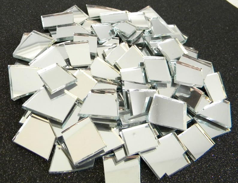 May include: A pile of small, square, silver mirror tiles. The tiles are various sizes and are arranged in a random pattern.