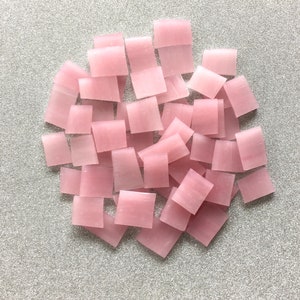 May include: A collection of pink, square-shaped tiles, arranged in a random pattern. The tiles are made of a translucent material, and they have a slightly iridescent sheen.