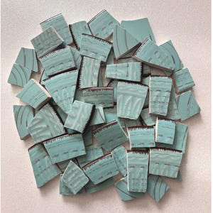 May include: A collection of irregularly shaped, turquoise-colored ceramic tiles with a distressed, textured appearance. The tiles have dark brown edges and a pattern of horizontal lines. The pieces are scattered on a white surface.