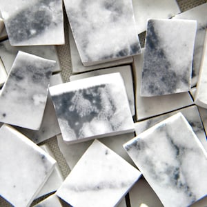 May include: A collection of small, white marble tiles with gray veining. The tiles are irregular in shape and size, and some have rounded edges.