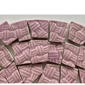 May include: A collection of broken, irregular-shaped tiles in a soft lavender hue. Each tile features a raised, woven texture, creating a tactile and visually interesting surface. The tiles are arranged in a scattered pattern, suggesting a mosaic or craft project.