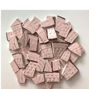 May include: A pile of pink ceramic tile pieces with a brown and white pattern. The tiles are irregular in shape and size, and some have a rough edge.