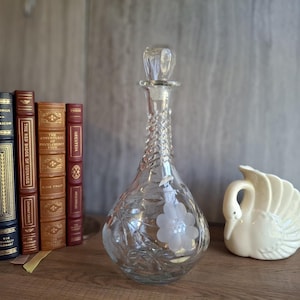 May include: A white ceramic mug with a black handle and the text "But first, coffee" in a black, handwritten-style font. The mug is on a white surface.