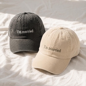 Peut inclure: Deux casquettes de baseball, l'une en gris anthracite délavé et l'autre en beige clair, portant toutes deux le texte brodé "I'm married" dans une police simple sur le panneau avant. Chaque casquette a une visière courbée et des œillets.