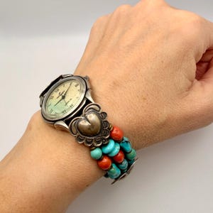 Può includere: Orologio color argento con quadrante color crema e numeri romani. Il cinturino dell'orologio presenta un design a forma di cuore ed è decorato con perline turchesi e corallo. Un orologio unico in stile sud-occidentale.