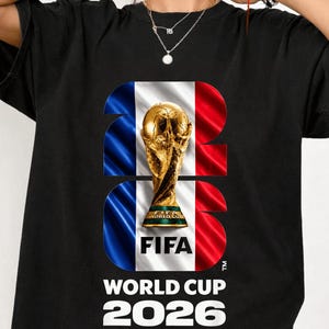 May include: A black t-shirt featuring a large graphic of the FIFA World Cup trophy centered within the number 2026. The background of the numbers displays the French flag in blue, white, and red. The text FIFA WORLD CUP 2026 is printed below.