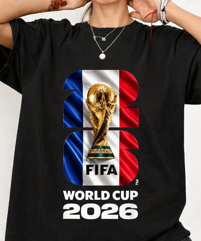 May include: A black t-shirt featuring a large graphic of the FIFA World Cup trophy centered within the number 2026. The background of the numbers displays the French flag in blue, white, and red. The text FIFA WORLD CUP 2026 is printed below.