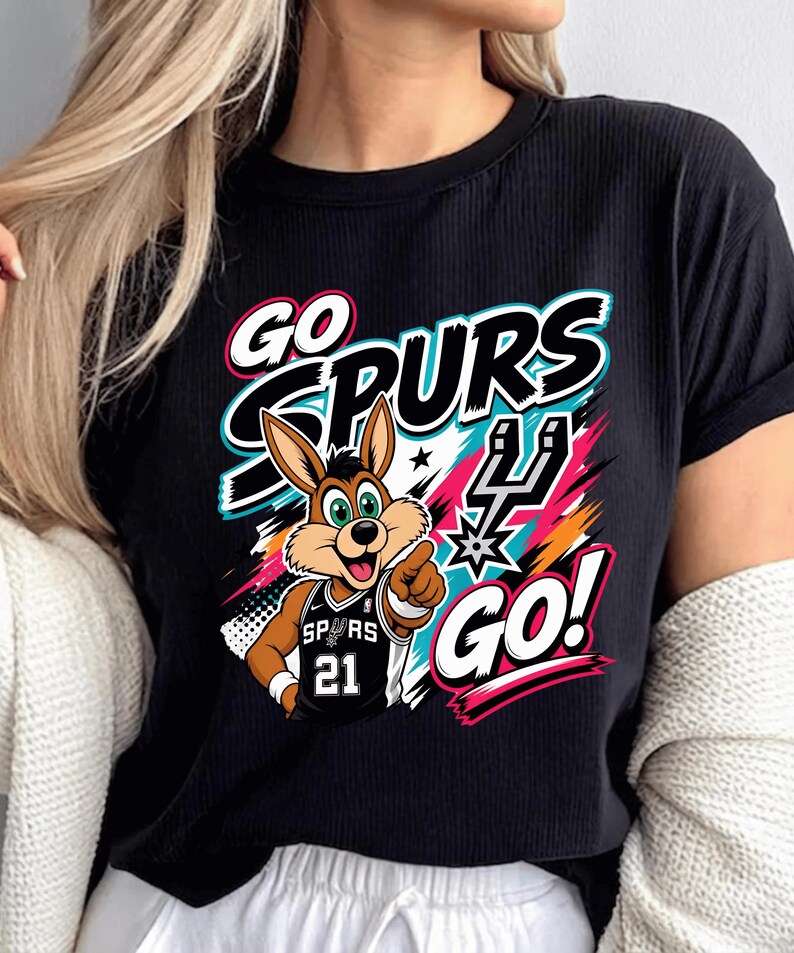 May include: Black t-shirt featuring a cartoon jackrabbit wearing a Spurs jersey with the number 21. The shirt has the words "GO SPURS GO!" in a colorful design with teal, pink, and orange accents. The jackrabbit is pointing.