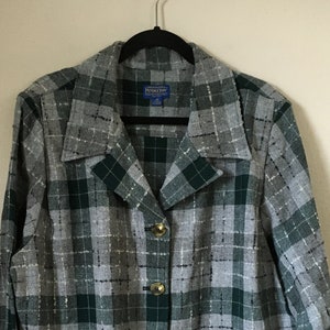 May include: A gray, green, and white plaid jacket with gold buttons and two front pockets. The jacket is hanging on a black hanger. The label reads "Pendleton".
