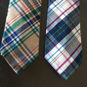 May include: Two plaid neckties, one with a beige, blue, green, and orange plaid pattern, and the other with a white, blue, green, and pink plaid pattern.