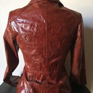 May include: A brown leather jacket with a collared neckline and long sleeves. The jacket has a fitted silhouette and a smooth, glossy finish.