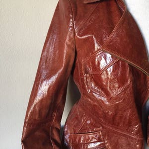 May include: A brown leather jacket with a zipper closure and multiple pockets. The jacket has a shiny finish and a classic design.