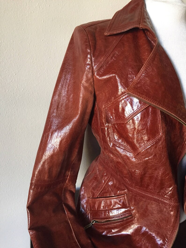 May include: A brown leather jacket with a zipper closure and multiple pockets. The jacket has a shiny finish and a classic design.