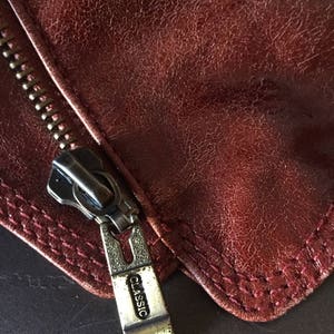 May include: Close-up of a zipper pull on a brown leather jacket. The zipper pull is silver and has the word "CLASSIC" engraved on it.