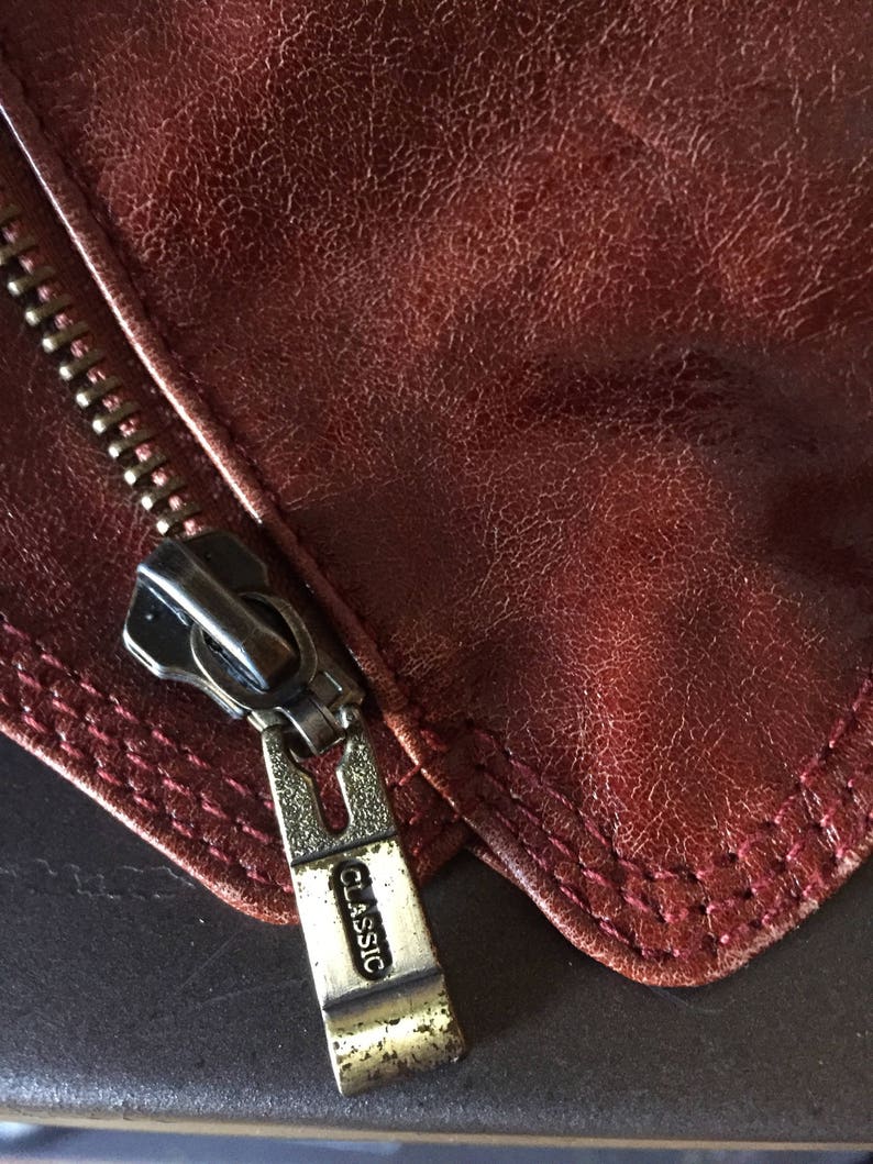 May include: Close-up of a zipper pull on a brown leather jacket. The zipper pull is silver and has the word "CLASSIC" engraved on it.