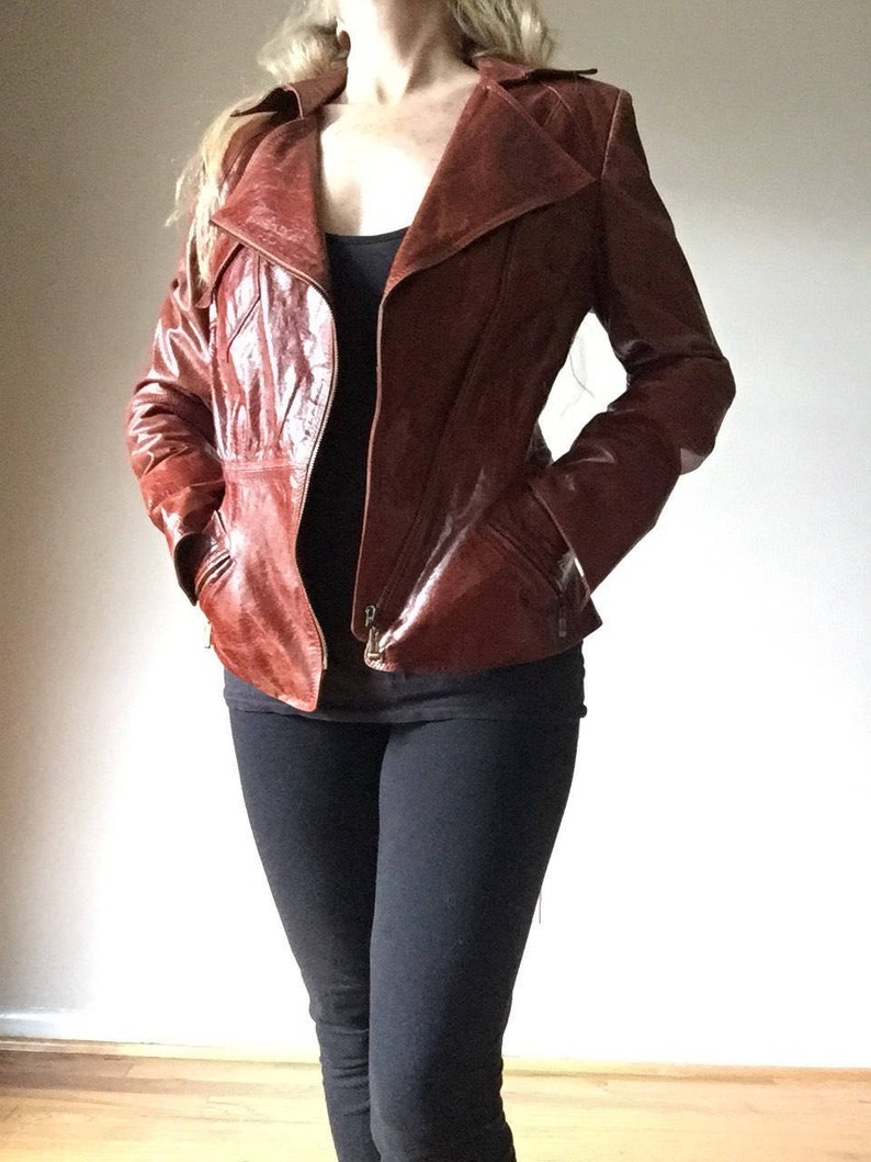 May include: A brown leather jacket with a zipper closure and a collar. The jacket has a fitted silhouette and is made of a smooth, shiny leather.