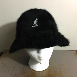 Op de afbeelding: Een zwarte Kangol-emmerhoed met een zachte, donzige textuur. De hoed heeft een klein, wit geborduurd kangoeroelogo. De hoed wordt gepresenteerd op een witte mannequinhoofd.