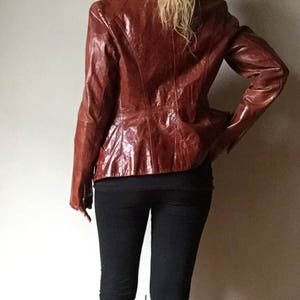 May include: A brown leather jacket with a zipper closure. The jacket has a slightly fitted silhouette and a collar.