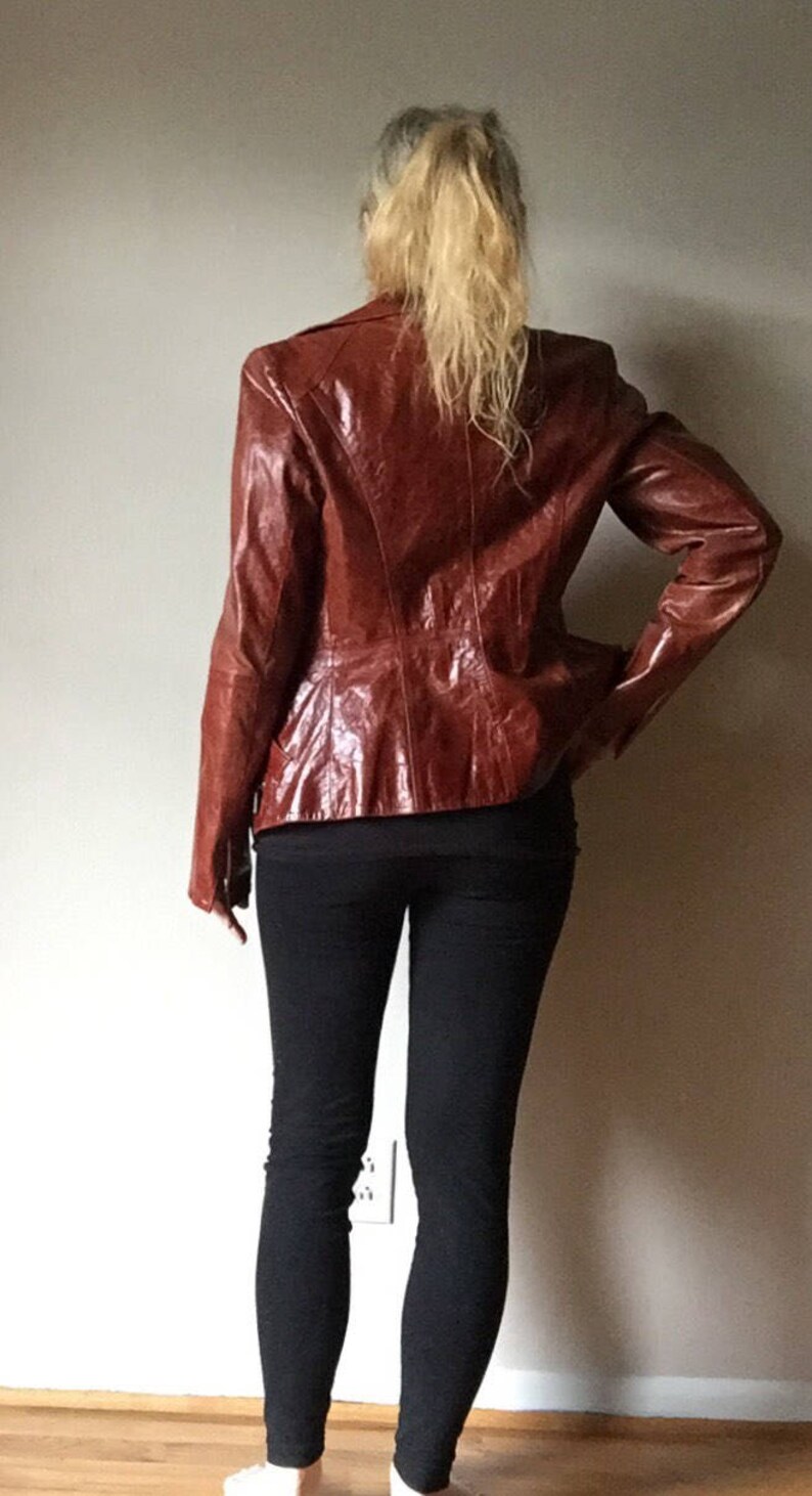May include: A brown leather jacket with a zipper closure. The jacket has a slightly fitted silhouette and a collar.