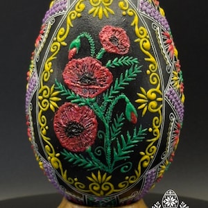Könnte beinhalten: Ein schwarzes Ei mit erhabenen, texturierten Reliefmustern, die rote Mohnblumen mit grünen Stielen und Blättern zeigen, umgeben von gelben und violetten geometrischen und floralen Motiven. Am Fuß steht der Text Atelier Zestrea Anamaria Buraciuc.