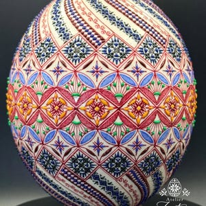 Pode incluir: Um ovo decorado com padrões geométricos intrincados em vermelho, azul, amarelo e verde. A superfície apresenta linhas texturizadas em relevo que formam diamantes, estrelas e motivos florais. O texto "Atelier Zestrea Anamaria Buraciuc" é visível.