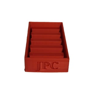 Könnte beinhalten: Ein roter, mehrstufiger Organizer mit rechteckiger Basis und mehreren horizontalen Ablagen. Der Organizer hat die Buchstaben "JPC" auf der Vorderseite eingeprägt. Die Ablagen sind gleichmäßig angeordnet.