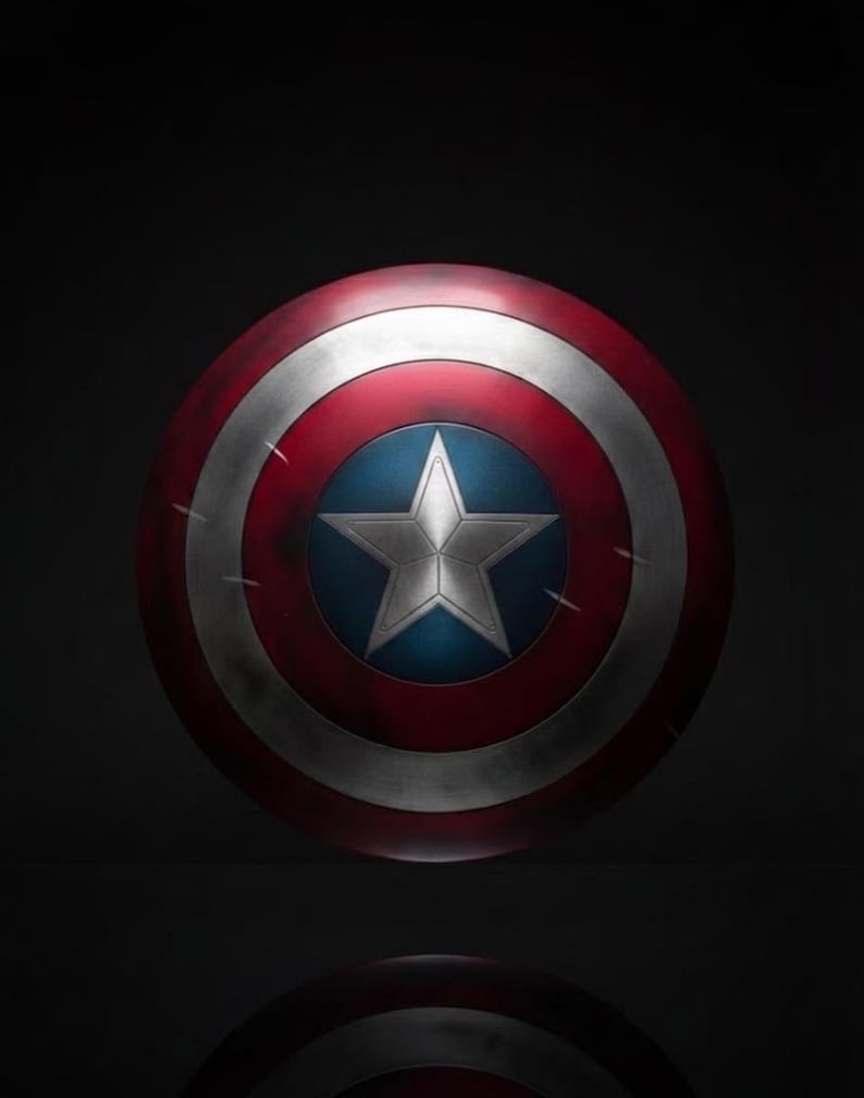May include: A round shield with a red, white, and blue color scheme. The shield features a white star on a blue center, surrounded by concentric red and white bands. The shield has a distressed, battle-worn appearance.