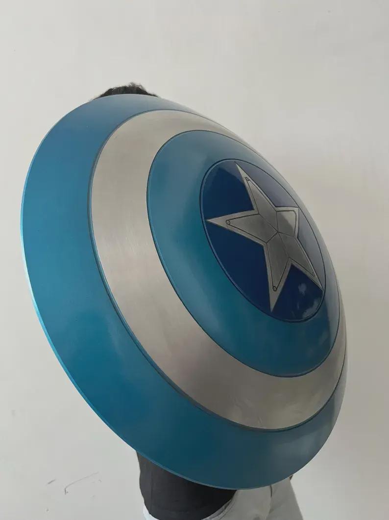 May include: A blue, silver, and white shield with a star emblem. The shield is round with concentric circles of colour. The central star is silver. The shield is a prop or costume accessory.