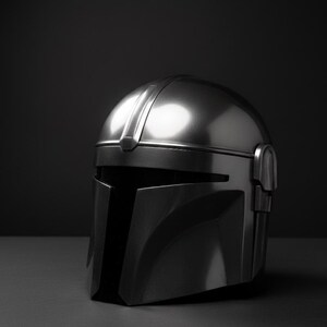 May include: A silver metallic helmet with a T-shaped visor and a rounded top. The helmet has a sleek, futuristic design, set against a dark background. It is likely a prop or collectible item.