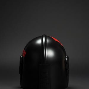 Op de afbeelding: Een zwarte helm met rode accenten. De helm heeft een gladde, glanzende afwerking en een gestroomlijnd ontwerp. Rode markeringen zijn zichtbaar op de boven- en zijkant. De helm is waarschijnlijk voor bescherming.