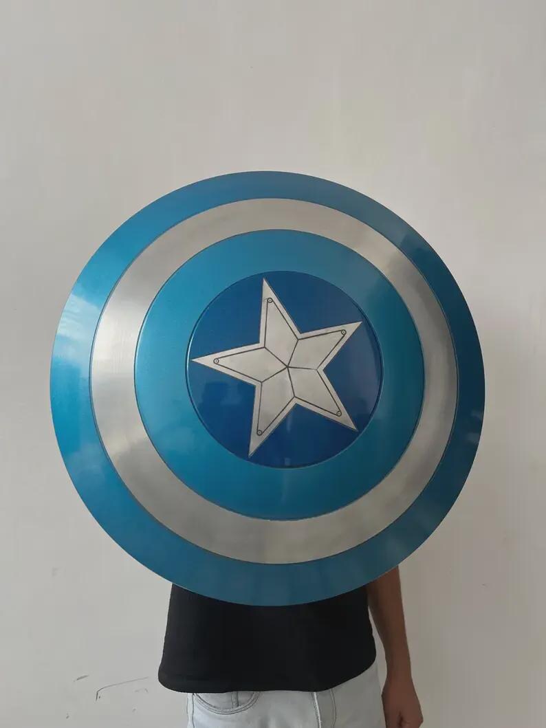 May include: A circular shield featuring a blue and silver design. The shield has a large white star at its centre, encircled by bands of blue and silver. This shield is likely a prop or costume accessory.