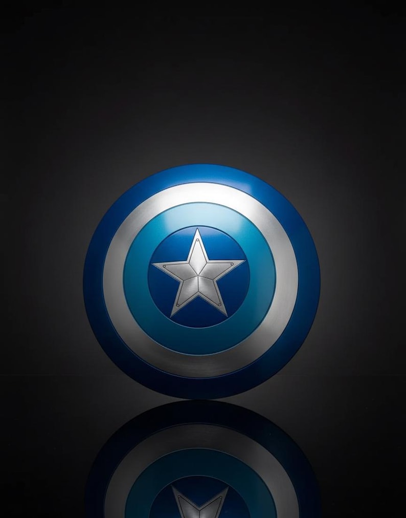 May include: A circular shield in blue, silver, and white, featuring a central silver star. The shield has concentric rings of different blue and silver tones. The shield is round and appears to be made of metal.