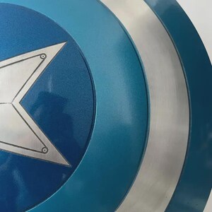May include: A close-up of a blue and silver shield with a white star in the center. The shield has a circular design with concentric rings of blue and silver. The star has a silver outline and is centered on a dark blue background.