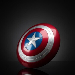 Puede incluir: Un escudo del Capit&aacute;n Am&eacute;rica rojo, blanco y azul. El escudo tiene un dise&ntilde;o circular con una estrella blanca sobre un c&iacute;rculo azul en el centro, rodeado de anillos conc&eacute;ntricos blancos y plateados. El escudo est&aacute; ligeramente inclinado, con su reflejo visible.
