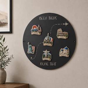 May include: A circular black wall plaque with the text BEEN THERE DONE THAT. It features a dashed flight path and six colorful 3D magnets representing Japan, USA, France, Brazil, Italy, and Greece, each with iconic landmarks and country names.