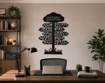 May include: A black wall-mounted sign featuring the text "OUR FAMILY ADVENTURES" in a cloud-shaped top, with four horizontal arrow-shaped boards below. Each arrow is decorated with numerous small, colorful circular travel-themed patches.