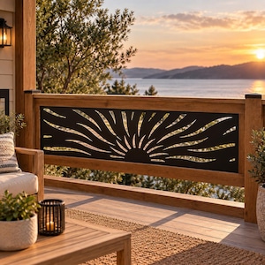 May include: A rectangular black metal railing insert featuring a laser-cut sunburst design with radiating curved lines. The panel is mounted within a wooden frame on a deck, positioned horizontally between two vertical wooden posts.