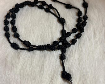 May include: Black knotted rosary necklace with a silver pendant featuring a stylized serpent design. The necklace is made of black cord with evenly spaced knots. The pendant hangs from the bottom of the necklace.