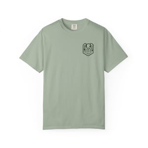 Puede incluir: Camiseta verde salvia de manga corta con cuello redondo. La camiseta presenta un gráfico negro en la parte superior izquierda del pecho que dice "LRI USEC". La camiseta está hecha de un material suave y cómodo.