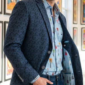 Peut inclure: Un blazer bleu marine orné de notes de musique, associé à une chemise bleu clair ornée d'une guitare. Le blazer est porté sur une chemise rayée bleu clair et un jean bleu foncé. La doublure du blazer présente également une impression de guitare.