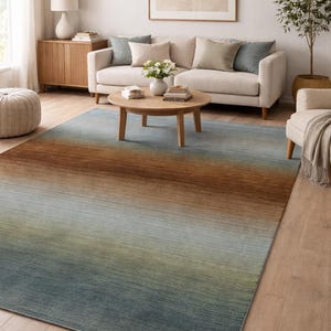May include: A rectangular area rug with a gradient design. The rug transitions from a brown hue at the top to shades of green and blue at the bottom. The rug is placed on a wooden floor in a living room setting.