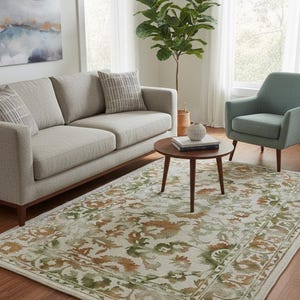 May include: A living room scene featuring a light gray sofa, a teal armchair, and a round wooden coffee table. A patterned rug with green and brown floral designs covers the floor. A large plant sits in the corner.