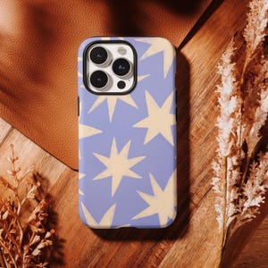 May include: A phone case with a light blue background and a pattern of cream-colored star shapes. The case has a black border and a camera cutout. The phone case is on a wooden surface.