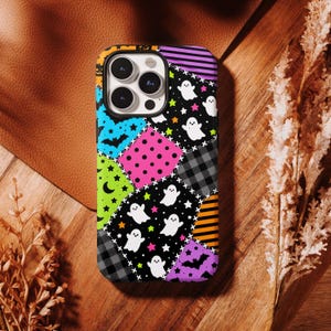 May include: A smartphone case featuring a patchwork design of various Halloween-themed patterns including white ghosts, black bats, orange and black stripes, pink polka dots, grey plaid, and neon green stars on a black background.