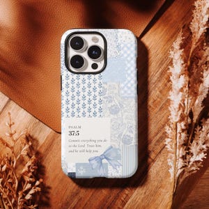 Può includere: Una custodia per smartphone con un design patchwork azzurro e bianco con motivi floreali, a quadretti e a foglie. Un pannello rettangolare bianco centrale mostra il testo Psalm 37:5, Commit everything you do to the Lord. Trust him, and he will help you, accompagnato da una piccola illustrazione di un fiocco blu.